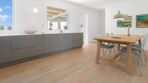 A modern kitchen with grey cabinets, a wooden dining table, and a large window. - 5 Star Holiday Home in Lokken (Lokken)