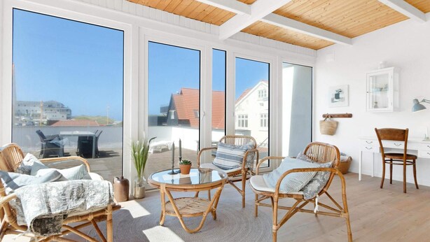 A bright room with large windows, wicker furniture, and a wooden ceiling. - 5 Star Holiday Home in Lokken (Lokken)
