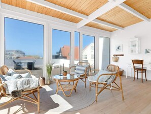 A bright room with large windows, wicker furniture, and a wooden ceiling. - 5 Star Holiday Home in Lokken (Lokken)