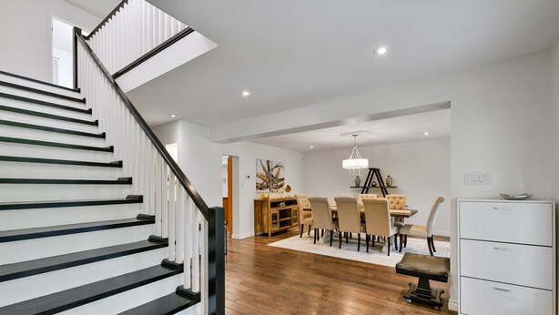 Een modern interieur met een houten trap, een eetgedeelte met een kroonluchter en een witte kast.