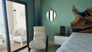A bedroom with a bed, a chair, a nightstand, a mirror, and a view of the outside. - Rent a home away from home in front of the Best View of beautiful Samaná Bay! (Samana)