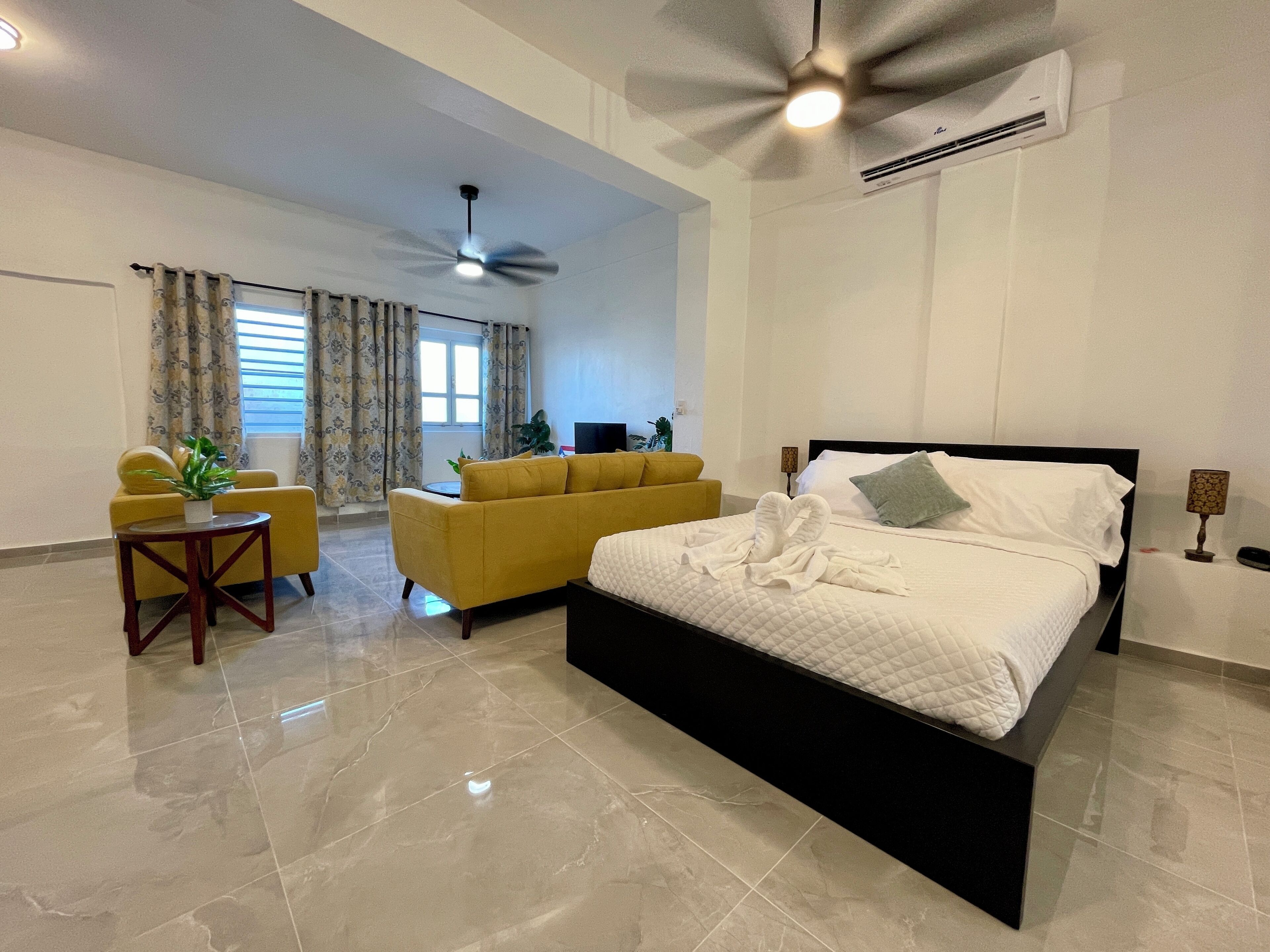 Una habitación de hotel moderna con una cama grande, un sofá, una mesita y un ventilador de techo.