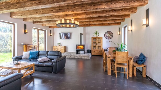 Ein großzügiger Wohnbereich mit Kamin aus Stein, Holzbalkendecke und einer modernen Couch.