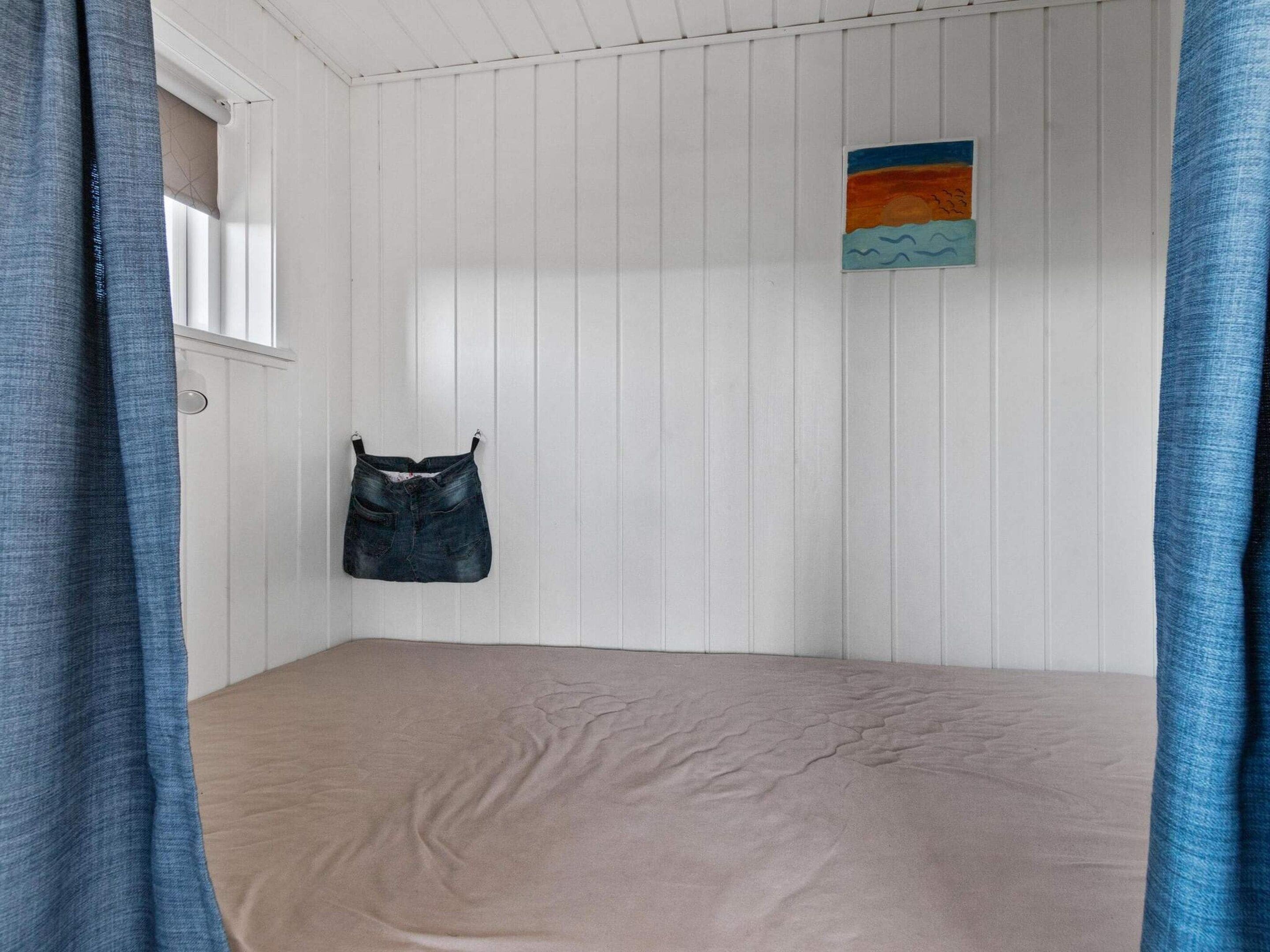A room with a bed, a hanging bag, and a painting on the wall.