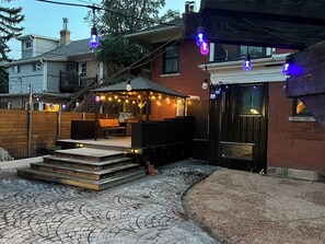 A backyard with a barbecue area, steps leading to a deck, and string lights.