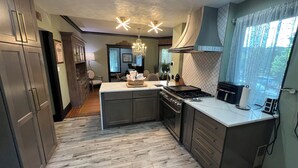 Uma cozinha moderna com uma ilha central, armários escuros e uma janela grande com cortinas.