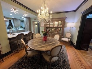 A dining area with a round wooden table, six chairs, a chandelier, and a patterned rug.
