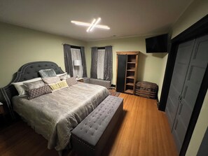 A bedroom with a large bed, a bench, a wardrobe, and a TV mounted on the wall.