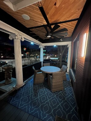 A covered outdoor patio with a round table and wicker chairs, a decorative column, and a view of the street at night.