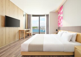 A hotel room with a large bed, a desk, a TV, and a view of the sea.