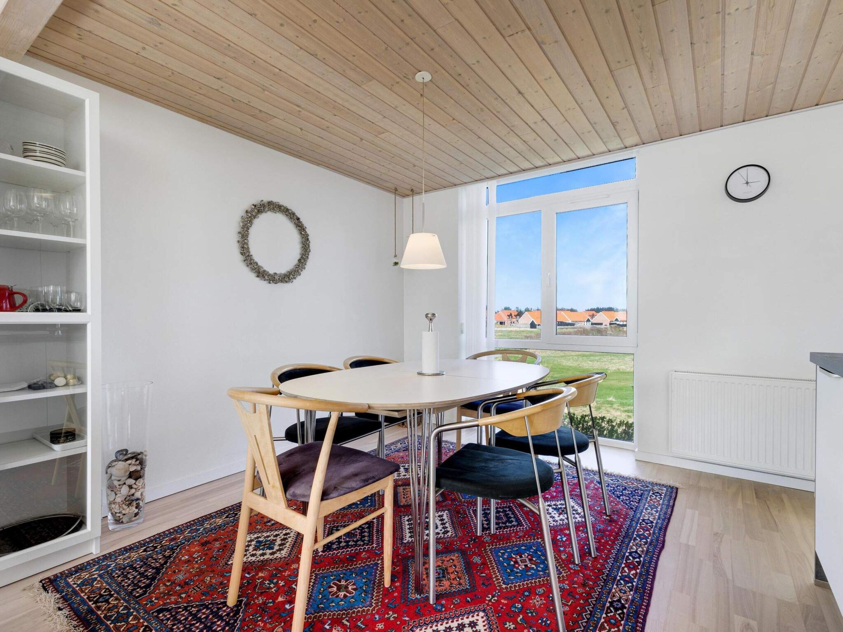 Une pièce avec une table ronde, des chaises, une lampe, une bibliothèque, une couronne décorative et une fenêtre donnant sur un paysage.