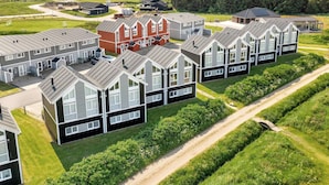 A residential area with modern houses, a central building with a red facade, and a view of the sea in the background. - 5 Star Holiday Home in Lokken (Lokken)