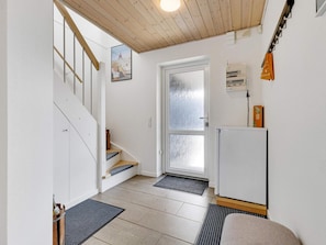 A hallway with a wooden staircase, a door with frosted glass, a white wall, and a small refrigerator.