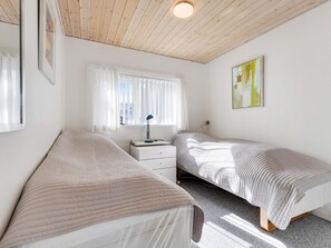 A bedroom with two single beds, a nightstand, a desk, and a window with curtains.