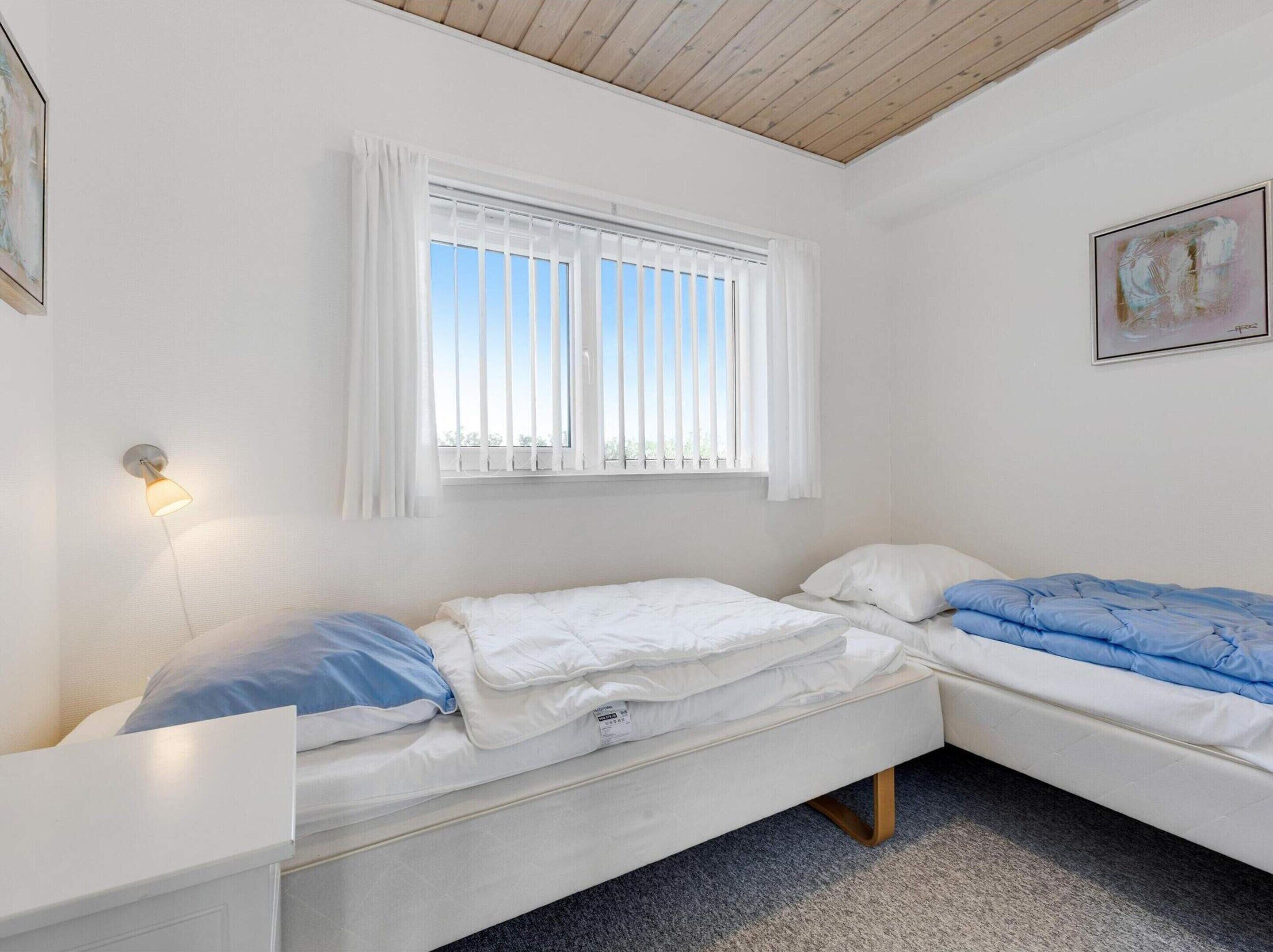 Una sistemazione piccola e singola con un letto, un comodino, una finestra con tende e un quadro appeso al muro.