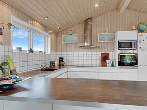 Eine moderne Küche mit Holzbalkendecke, weißen Schränken, einer Edelstahl-Dunstabzugshaube, einer Mikrowelle und einer Kaffeemaschine.