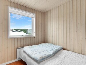 Ein Schlafzimmer mit einem Einzelbett, einem Fenster mit Blick auf ein Gebäude und Bäume sowie Holzwänden.