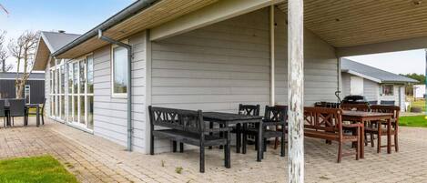 A covered outdoor patio with tables and chairs, a barbecue grill, and a grassy area.