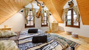 Un dormitorio acogedor en el ático, con techo inclinado, vigas de madera, una cama con ropa de cama estampada, un aparador y dos cornamentas de ciervo montadas en la pared.