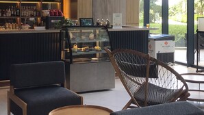 A modern bar area with seating, a display case, and a large window offering a view of greenery. - Ruby Provided Arena Cam Ranh (Bac Cam Ranh)