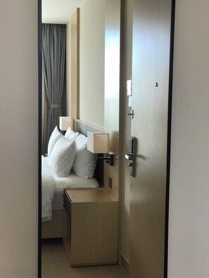 A hotel room with a bed, a nightstand, a lamp, a mirror, and a door. - Ruby Provided Arena Cam Ranh (Bac Cam Ranh)