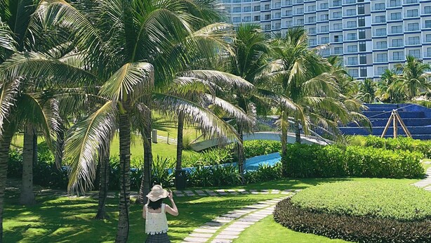 A modern hotel with a curved facade, surrounded by palm trees and a well-maintained garden. - Ruby Provided Arena Cam Ranh (Bac Cam Ranh)