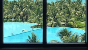 A view of a swimming pool surrounded by palm trees, with a clear blue ocean and boats in the distance. - Ruby Provided Arena Cam Ranh (Bac Cam Ranh)