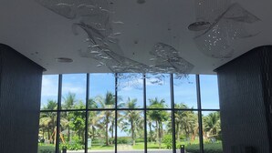 A spacious lobby with large windows, a modern ceiling design, and a view of palm trees and greenery outside. - Ruby Provided Arena Cam Ranh (Bac Cam Ranh)
