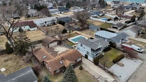 An aerial view of a residential area with houses, a swimming pool, and a beach in the background.