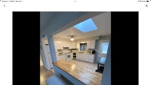 A modern kitchen with a skylight, white cabinets, and a wooden countertop.