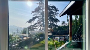 Une vue depuis une fenêtre, avec un ciel dégagé, un grand arbre et un jardin bien entretenu.