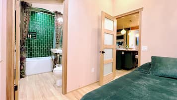 Een slaapkamer met een groen bed, een houten deur die leidt naar een badkamer met een groen betegelde muur, een wit toilet en een wastafel.