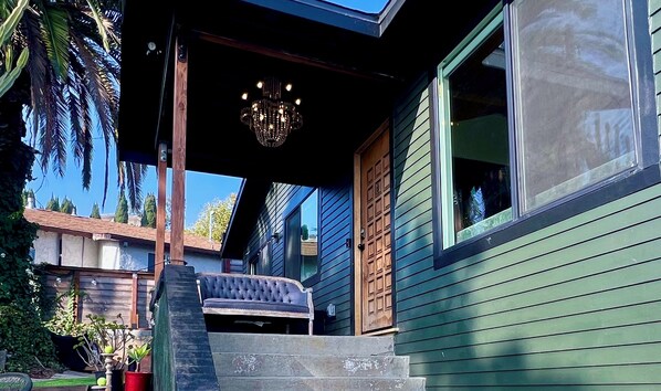 Una casa con porche cubierto, un candelabro y una escalera que lleva a la entrada.
