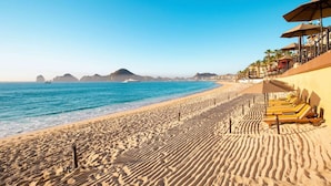 Ein Strand mit Liegestühlen und Sonnenschirmen, einem klaren blauen Himmel und einem ruhigen Meer.