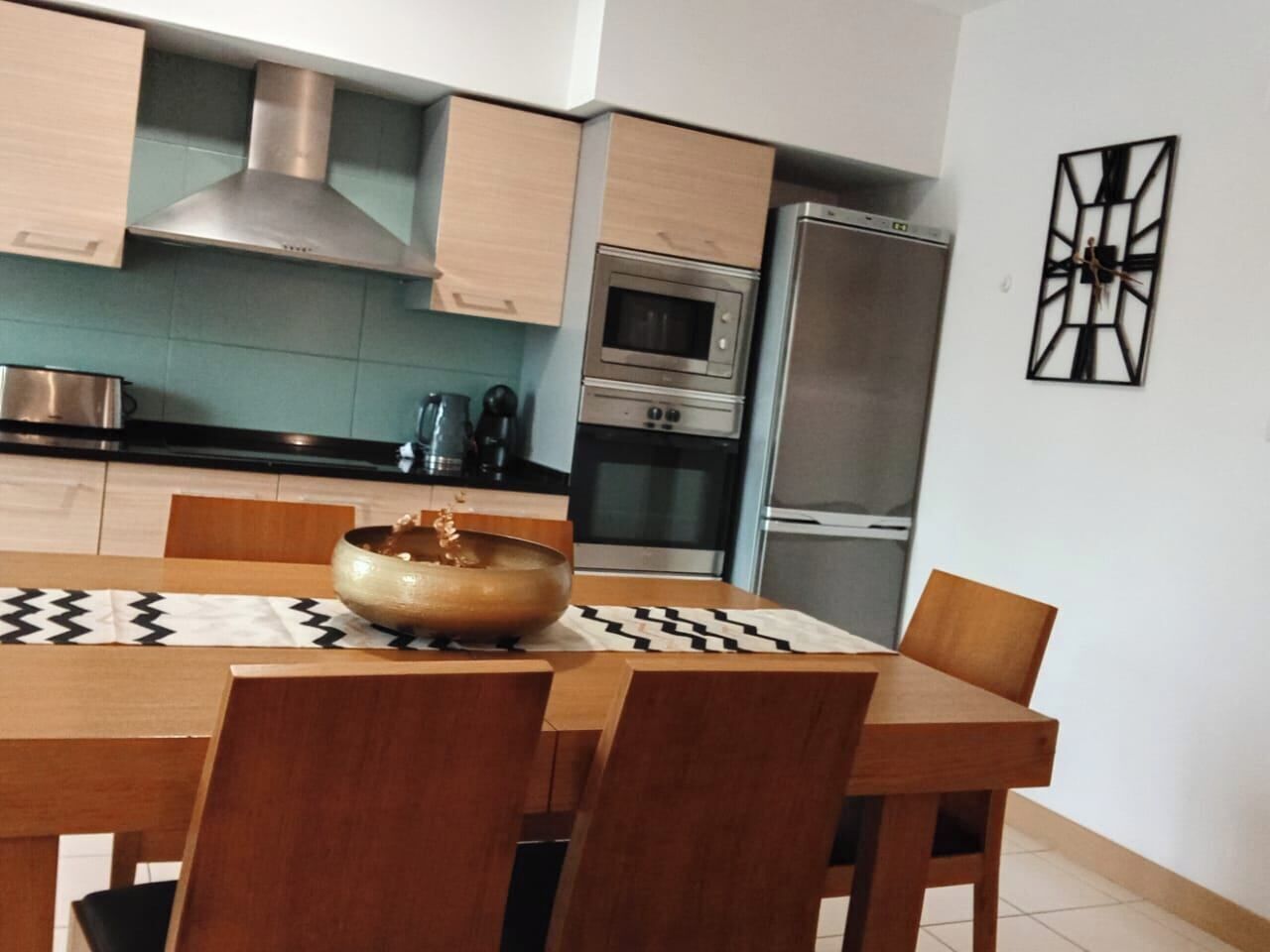 A modern kitchen with wooden cabinets, a stainless steel range hood, a microwave, and a refrigerator.