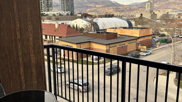 A balcony with a view of a parking lot, buildings, and mountains. - Quick walk to Lakeside Boardwalk and Downtown shops & restaurants! (Kelowna)