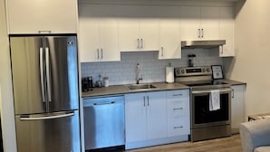 A modern kitchen with stainless steel appliances, white cabinets, and a tiled backsplash. - Quick walk to Lakeside Boardwalk and Downtown shops & restaurants! (Kelowna)