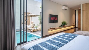 Una habitación de hotel moderna con una cama grande, un televisor montado en la pared y un ventanal corredero que da a una zona de piscina exterior.