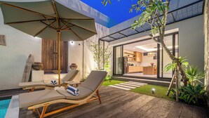 Un patio moderno al aire libre con sillones de descanso, piscina y vistas al interior de la casa.