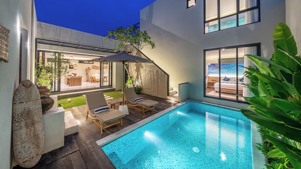 Un área de piscina moderna con sillones de descanso, una piscina pequeña y vista a un dormitorio con un amplio ventanal.
