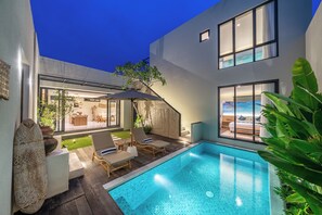 A modern pool area with lounge chairs, a small pool, and a view of a bedroom with a large window.