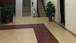 En rymlig entréhall med ett marmorgolv, en stor kristallkrona, en hiss och krukväxter.