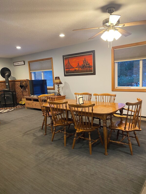 Un coin repas avec une table et des chaises en bois, un ventilateur de plafond, une cheminée et un tableau encadré au mur.