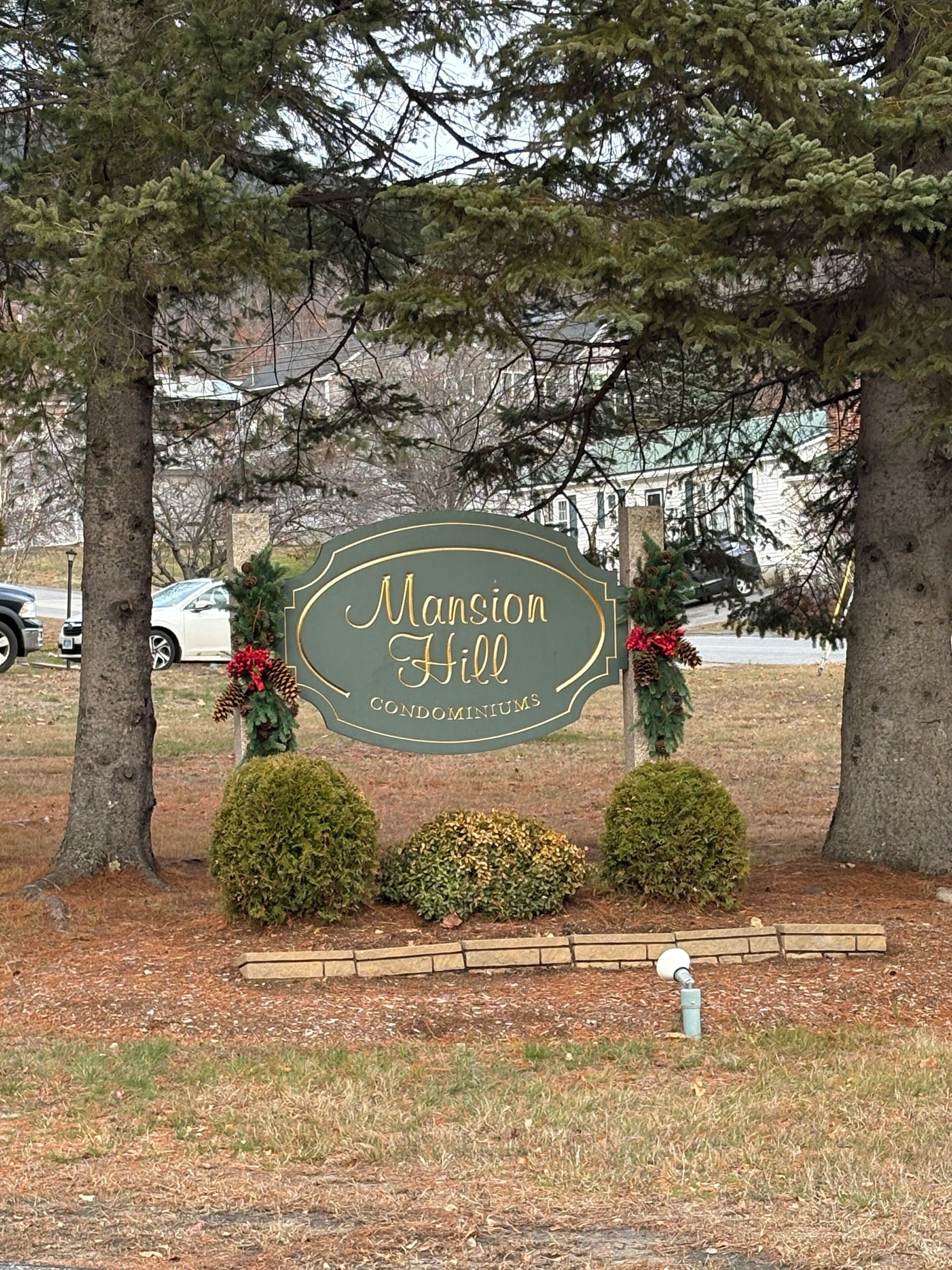 Schild für 'Mansion Hill Condominiums', umgeben von Bäumen und Sträuchern.