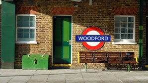 En byggnad av tegel med en grön dörr och gröna fönster, en bänk och en skylt med texten ”Woodford”.