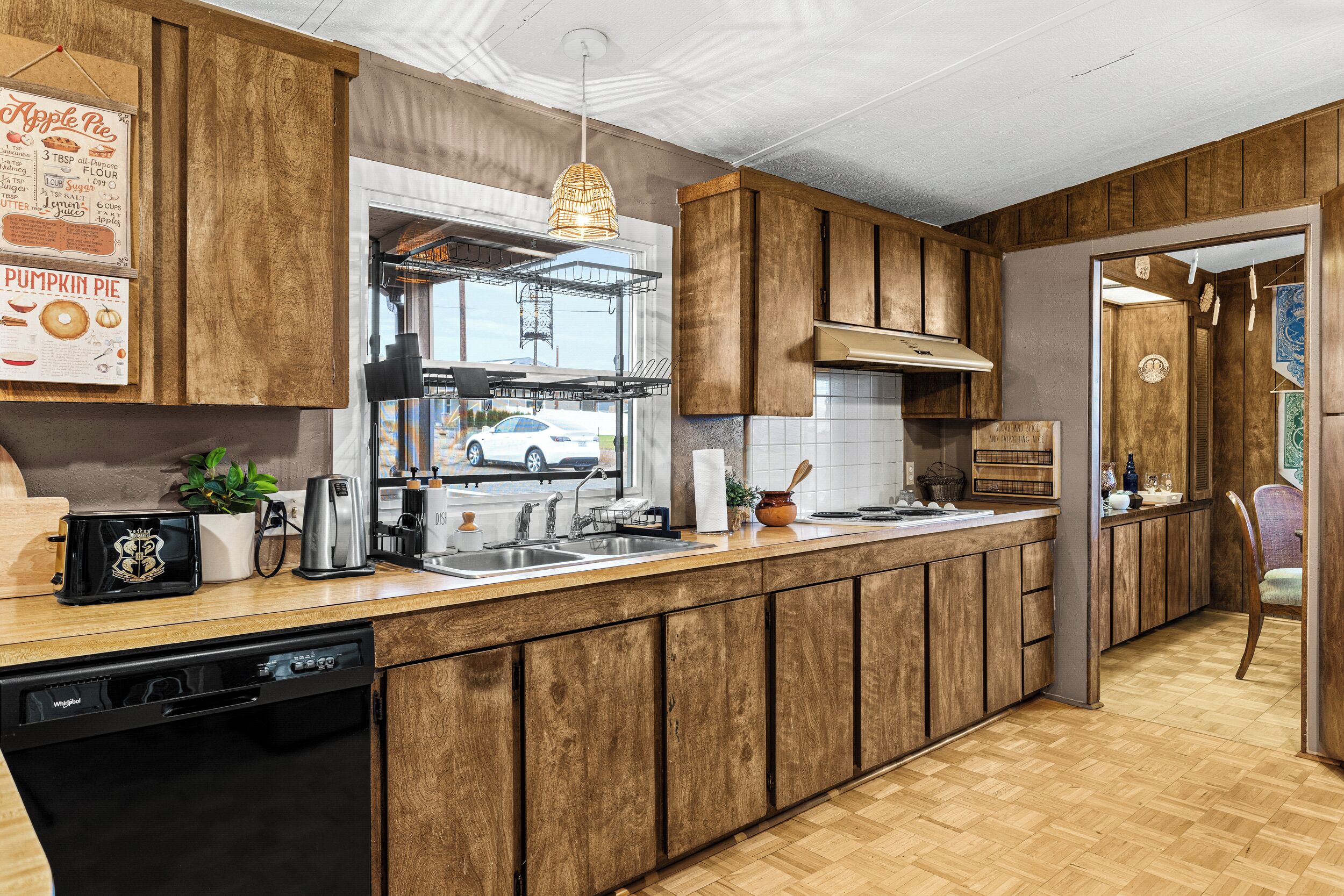 A modern kitchen with wooden cabinets, a built-in dishwasher, and a large window overlooking the street.