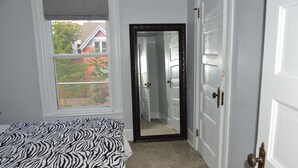 Un dormitorio con una colcha de estampado de cebra, un espejo grande y vistas a una casa roja a través de una ventana.