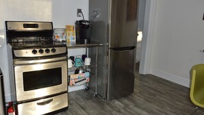 Una cocina con estufa, horno y refrigerador de acero inoxidable, una cafetera y un estante con utensilios de cocina.