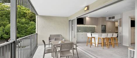 A modern kitchen with a bar area, a dining table with chairs, and a view of greenery outside.