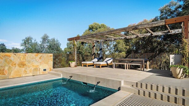 Une piscine agrémentée d’une pergola en bois, de chaises longues et d’un mur en pierre.